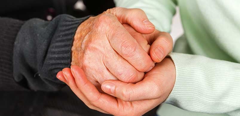 A closeup of an elderly person holding the hands of a younger person